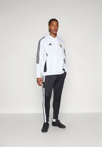 Completo sportivo Adidas, che include una felpa bianca con cappuccio, dettagli neri e logo, abbinata a pantaloni neri con strisce bianche ai lati.