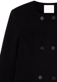 Svart dubbelknäppt jacka gjord av textil med struktur, med runda svarta knappar och rund halsringning, i en figurnära siluett.