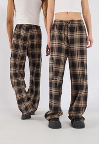 Bruine en zwarte geruite broek met een relaxte pasvorm, zijzakken, elastische tailleband en een trekkoord. Draagt met zwarte plateau-schoenen.