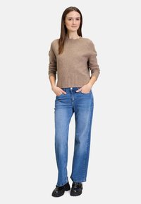 Lichtbruine gebreide trui met een geribde onderrand, gecombineerd met blauwe rechttoe rechtaan jeans en zwarte plateauschoenen met studs.