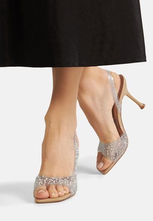Przezroczyste sandały na wysokim obcasie z beżową podeszwą i błyszczącymi srebrnymi ozdobami. Projekt z odkrytymi palcami i paskiem z tyłu zwiększa przewiewność.