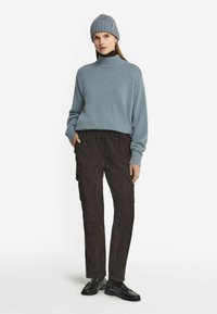 Ljusblå stickad tröja med hög krage, kombinerad med mörkbruna mocka cargo-byxor och svarta läderskor. Outfitten har en avslappnad passform.