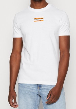 Witte katoenen T-shirt met korte mouwen en een ronde hals. Heeft een oranje en zwarte "Calvin Klein Jeans"-logo over de borst.