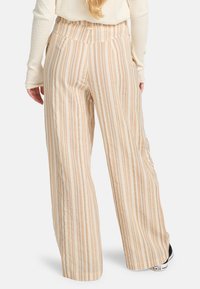 Pantaloni a gamba larga in crema con strisce verticali beige e arancione chiaro. Tessuto morbido con vita elastica e discreto dettaglio logo.