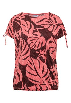 Femme vue de dos portant un haut à manches courtes imprimé de feuilles tropicales rose et rouge foncé et un jean bleu clair.
