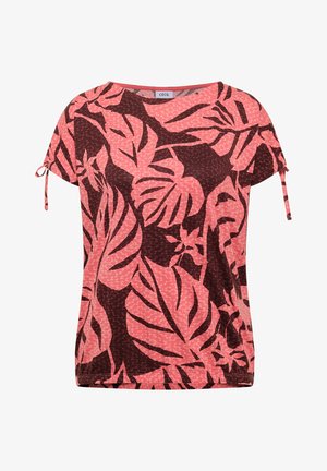 Femme vue de dos portant un haut à manches courtes imprimé de feuilles tropicales rose et rouge foncé et un jean bleu clair.