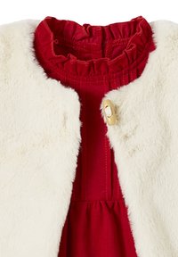 Weiße Kunstfell-Weste mit einem einzelnen Toggle-Button über einem roten, gestuften Hochkragenkleid mit gerafftem Bund.