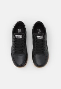 Para czarnych sneakersów Skechers z czarnymi sznurowadłami, białym logo na języku i boku oraz brązowymi gumowymi podeszwami, widziana z góry.