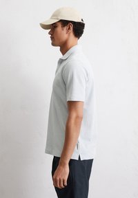 Lichtblauwe polo met een opstaande kraag, korte mouwen, zijsplitten en een subtiele textuur. Gekocht met een beige pet.