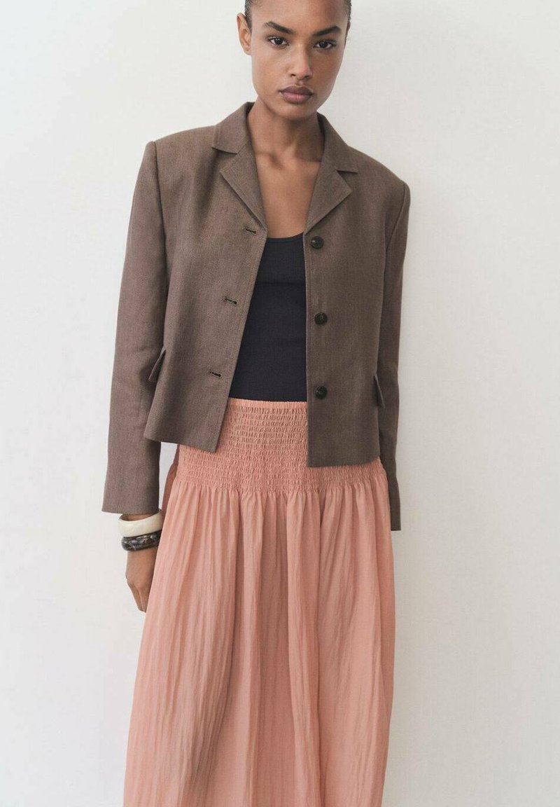 Blazer corto marrone con bottoni, abbinato a una gonna rosa smock. Tessuto con una consistenza liscia, design semplice e accenti minimalisti.