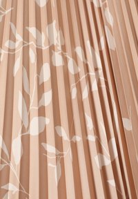 Tissu plissé en pêche doux, avec un subtil motif de feuilles blanches. Texture lisse avec des plis verticaux réguliers, créant profondeur et dimension.