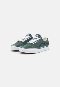 Zelené semišové sneakers s bílými tkaničkami, kontrastním prošíváním a černým bočním pruhem. Podešev je bílá a má hladkou texturu.