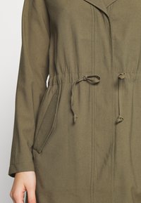 Olive green jacket with a tie waist, two side pockets, and a lapel collar. Made of smooth fabric with visible stitching details.