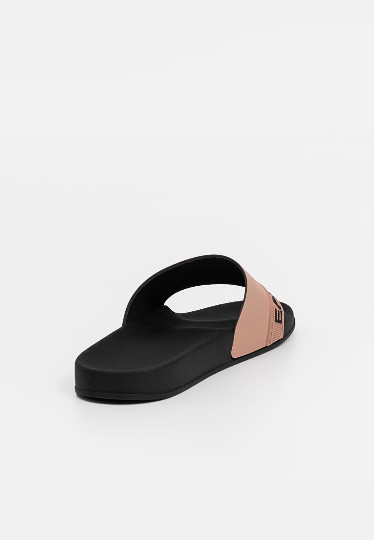 Sandalia tipo slide con una base negra y una tira suave de color rosa. La tira tiene un acabado texturizado y un acento de logotipo. Suela plana y diseño minimalista.