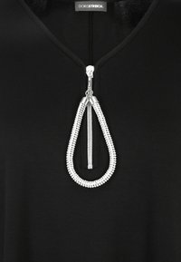 Schwarzes Kleidungsstück mit V-Ausschnitt und einem silbernen Reißverschluss in auffälliger Tropfenform, verziert mit Perlen, die einen strukturierten Akzent setzen.