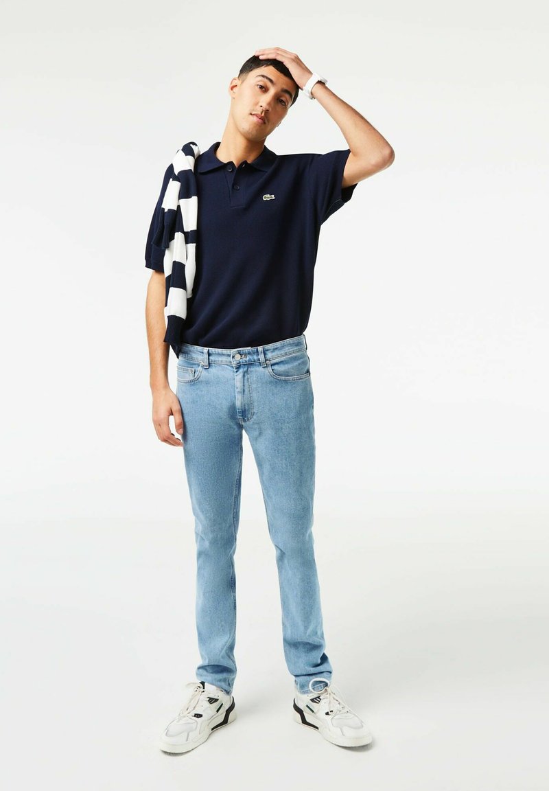 Polo en marine, jeans bleu clair, baskets blanches. Pull rayé drapé sur l'épaule. Look décontracté avec un design épuré.