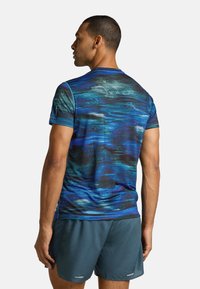 Camisa deportiva de manga corta con un patrón abstracto en azul y negro, hecha de una tela ligera; combinada con pantalones cortos oscuros.