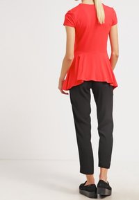 Röd peplumtop med korta ärmar, kombinerad med svarta smala byxor och kraftiga svarta skor, som visar upp ett slätt tyg och en avslappnad passform.