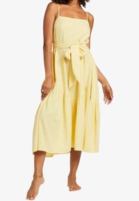 Gelbes, ärmelloses Kleid mit tailliertem Oberteil, Taillenbindegürtel und mehrlagigem Rock. Hergestellt aus leichtem Stoff, mit fließendem Design und weicher Textur.