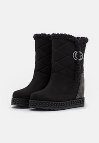 Sorte ankelstøvler med quiltet tekstur, imiteret pelskant, logodetalje og kilehæl med flettet design. Glat materiale over det hele.