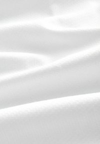 Simogató, fehér szövet finom redőkkel és enyhe szövött textúrával, amely lágy árnyékokat és kiemeléseket hoz létre.