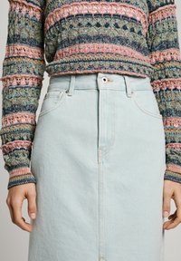 Lys blå denimskjørt med høy midje, med knappeåpning foran, sidelommer og kontraststing. Teksturert strikkegenser i flere farger.