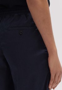 Granatowe spodnie o gładkiej fakturze, z tylną kieszenią z czarnym guzikiem i elastycznym pasem.