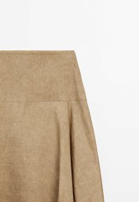 Jupe beige taille haute avec une couture près du haut et de subtils plis sur le côté droit, sur un fond blanc uni.
