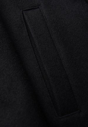 Tela de fieltro negro con una superficie texturizada y una abertura rectangular cosida en el material, presentando bordes y costuras limpias.