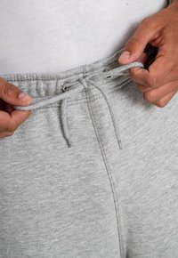 Graue Sweatpants mit einem Kordelzugbund. Der Stoff hat eine weiche Textur und verfügt über Metallösen zum Schnüren.