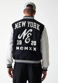 Navy and white varsity jacket with embroidered "NEW YORK," year "1920," and "MCMXX" on back. Ribbed cuffs and hem, wool body, leather sleeves.