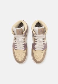 Paire de baskets montantes beige et mauve avec lacets blancs, bout perforé et logo de la marque visible sur la languette rembourrée.
