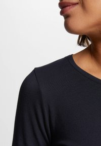 Dunkelblaues, geripptes T-Shirt mit rundem Ausschnitt, glatter Textur und tailliertem Design, das eine Nahaufnahme von Schulter und Ausschnitt zeigt.