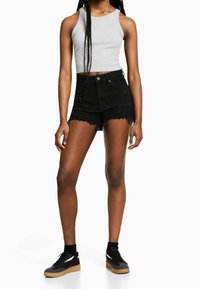 Top corto de canalé gris combinado con pantalones cortos de mezclilla negros desgastados, con dobladillo deshilachado y cintura alta. Zapatillas negras con suela de goma.