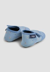Blå mjuka tygskor för bebisar med små segelbåtsmönster och rundad design, med en elastisk anklett för säker passform och en etikett.