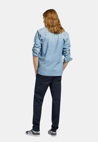 Camicetta di denim azzurro chiaro con maniche arrotolate, abbinata a pantaloni scuri e sneakers grigie con strisce bianche. Design semplice e casual.