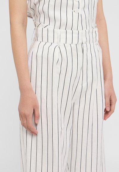Pantalons en lin blancs avec des rayures verticales noires. Dotés d'une taille ajustée et de poches latérales. Matériau léger et texture lisse.