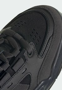 Μαύρο αθλητικό παπούτσι με συνδυασμό λείου δέρματος και υφασμάτινης σουέντ, ε�πίπεδες κορδόνες, διάτρητες λεπτομέρειες και μαξιλαρωμένο κολάρο.