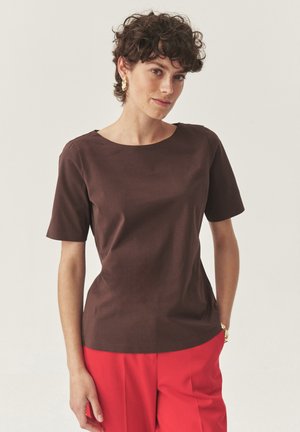 Top corto marrón de manga corta con un escote redondo, textura suave, diseño ajustado, combinado con pantalones rojos de cintura alta. Sin patrones notables.