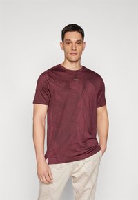 Camiseta de manga corta color marrón burdeos con patrón geométrico, escote redondo y sutil logo en el pecho, hecha de una tela suave.
