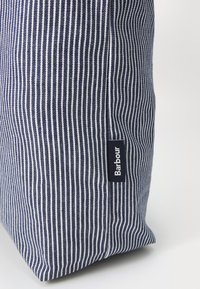 Csíkos sötétkék táska fehér vonalakkal, szövetből készült. Az oldalán egy kis fekete címke található, rajta fehér szöveggel: "Barbour".