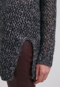 Mörkgrå stickad tröja med lös väv, med en sidoreva och strukturerad yta. Muddar på långa ärmar kompletterar den avslappnade passformen.