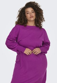 Magenta tröja med lång, puffärmad design och spetsdetaljer. Mjuk stickad struktur och rund halsringning, avslappnad passform.