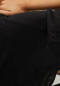 Schwarzes Stoffoberteil mit aufwendiger Stickerei am Saum. Glatte Textur mit lockerer Passform; kurze Ärmel und runder Ausschnitt.