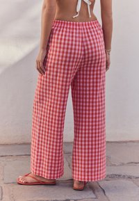 Röd- och vitrutiga vida byxor med texturerat tyg och resår i midjan, kombinerade med röda flip-flops.