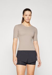 Kratki rukavi, uska majica od svijetlosmeđeg materijala, uparen s crnim sportskim šorcima s višeslojnim dizajnom. Glatka tekstura, minimalni detalji.