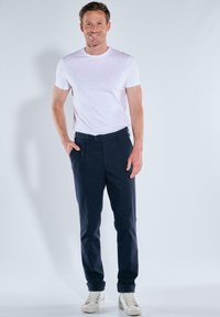 Navy chinos with a straight fit, cotton material, belt loops, front pockets, and tapered cuffs, paired with a plain white T-shirt and sneakers.