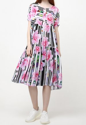 Kvinde iført en knælængde kjole med sorte og hvide lodrette striber og store pink blomsterprint, kombineret med hvide sneakers.