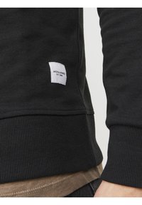 Felpa nera con maniche a costine e orlo, dotata di un'etichetta bianca sul lato che riporta la scritta "JACK & JONES EST. 1990." Texture morbida.