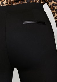 Czarne spodnie o sleek designie, z poziomym akcentem z czarnej sztucznej skóry na tylnej kieszeni, wykonane z gładkiego materiału.